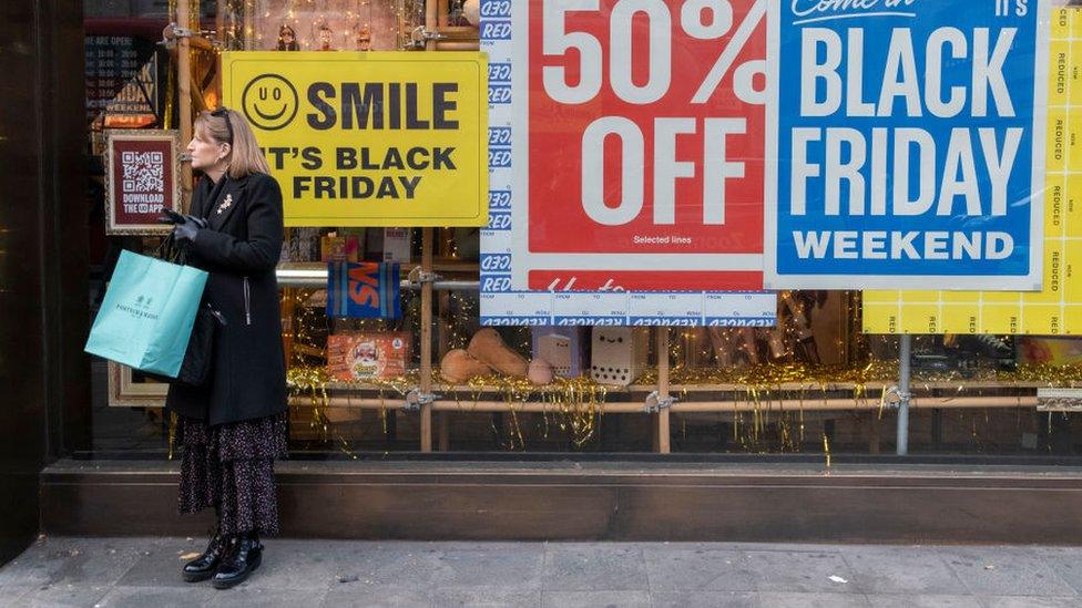 Woman standing outside of a store with Black Friday signage