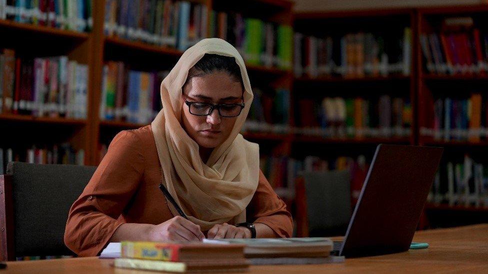 Wahida writing in a library