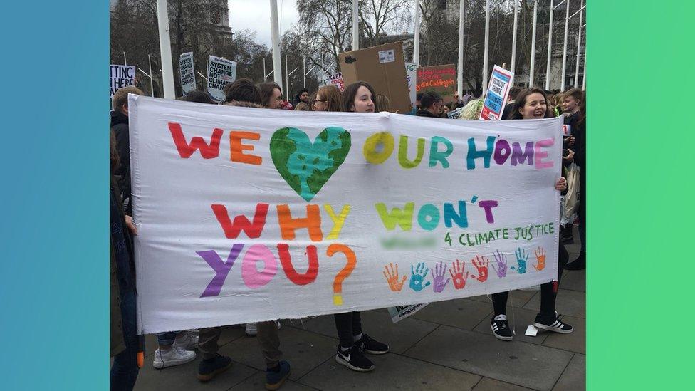 Students holding a sign saying "We love our home - why won't you?"