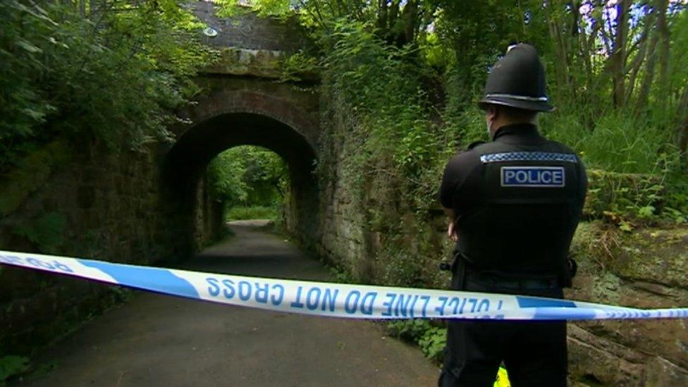 Police officer standing behind tape on footpath