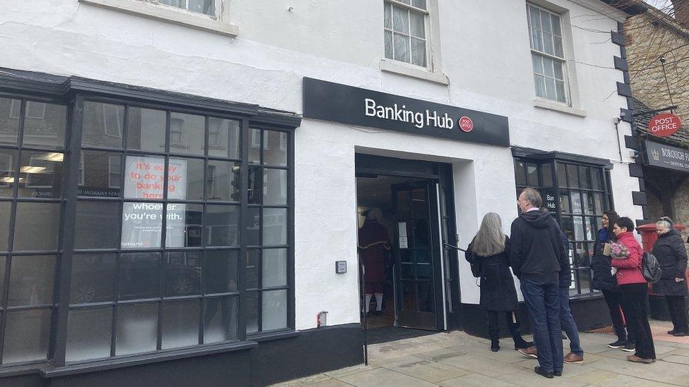 People outside the new banking hub, which is a white building with black latticed windows