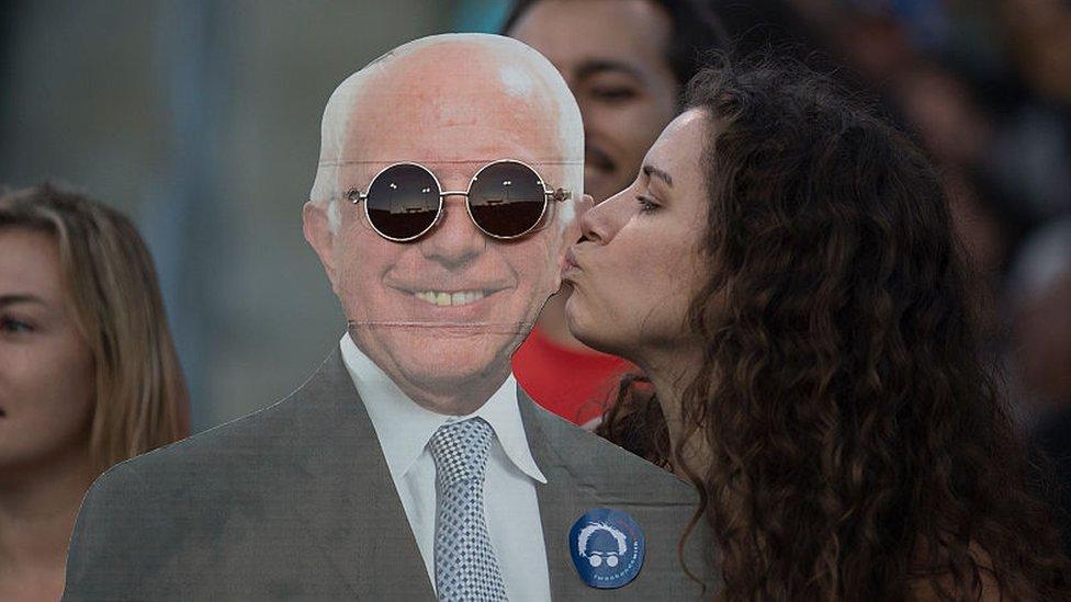 A woman kisses a cardboard cutout of Bernie Sanders.