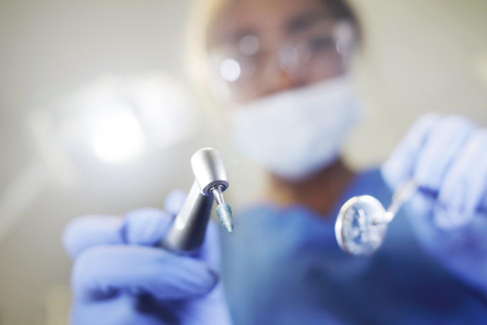 Dentist looking down on the camera holding tools.