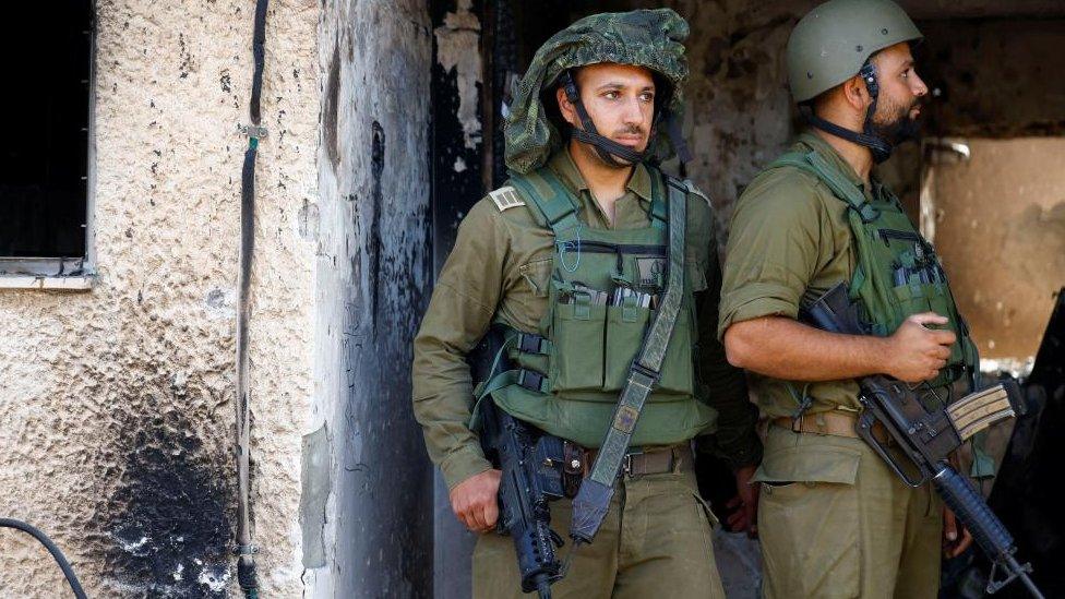 Soldiers look on near a destroyed home riddled with bullets, following the deadly October 7 attack by Hamas gunmen from the Gaza Strip, in Kibbutz Kfar Aza