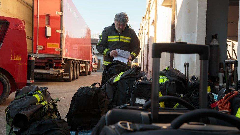 A firefighter stands near suitcases and checks a list