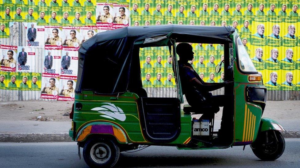 A bajaji (tuk-tuk) driver waits in traffic next to election posters in Dar es Salaam on 20 October 2015