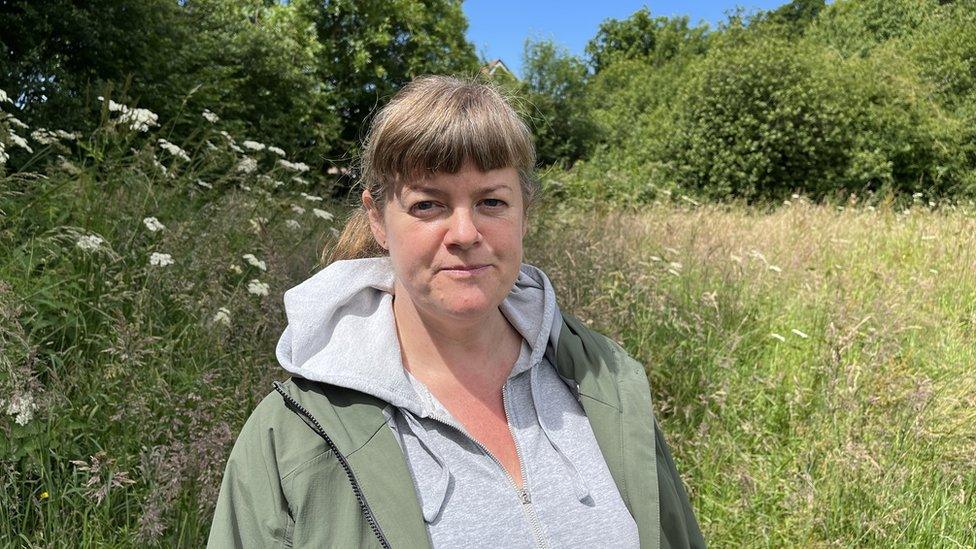 a woman in a green coat and grey hoodie in a wild field