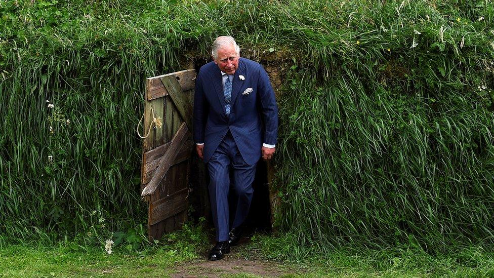 Prince Charles emerges from a recreation of a potato famine-era mud hut at University College Cork