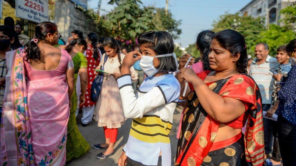 A mother ties a facemask on her daughter amid concerns over the spread of the COVID-19 coronavirus as she attends the first day of her tenth class examinations in Secunderabad, the twin city of Hyderabad, on March 19, 2020.