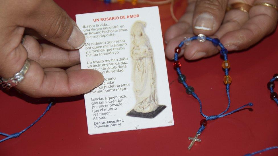 A woman holds up a prayer card and a handmade bracelet