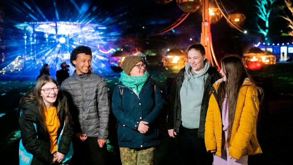 Group of people stood in front of In the Balance sculpture and a lit up bandstand