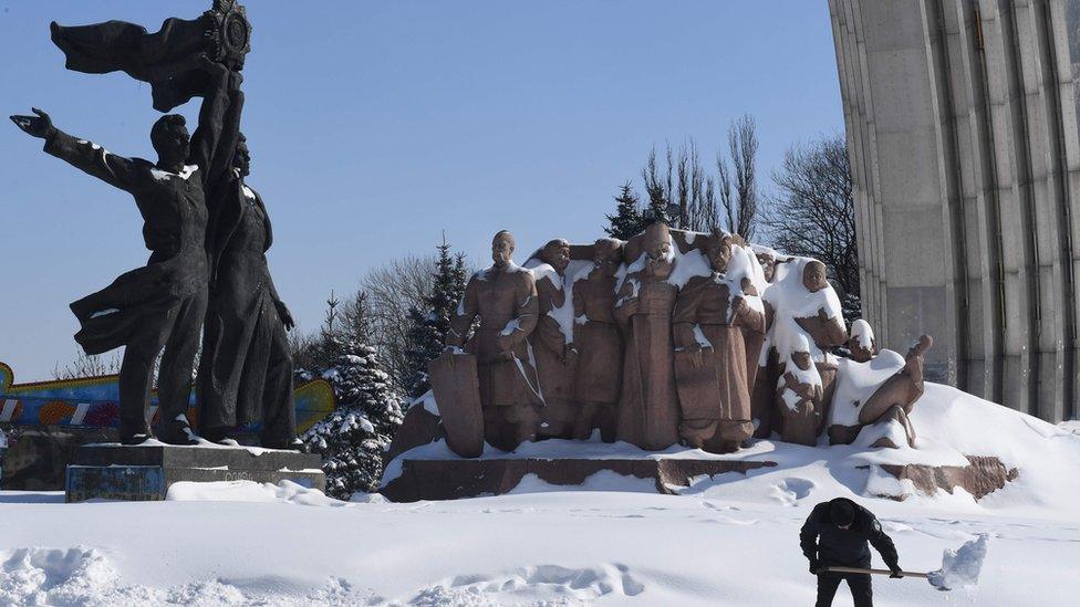 A communal worker cleans a road from a snow in front of Soviet era monument Ukraine and Russia union in Ukrainian capital of Kiev after heavy night snowfall on March 2, 2018