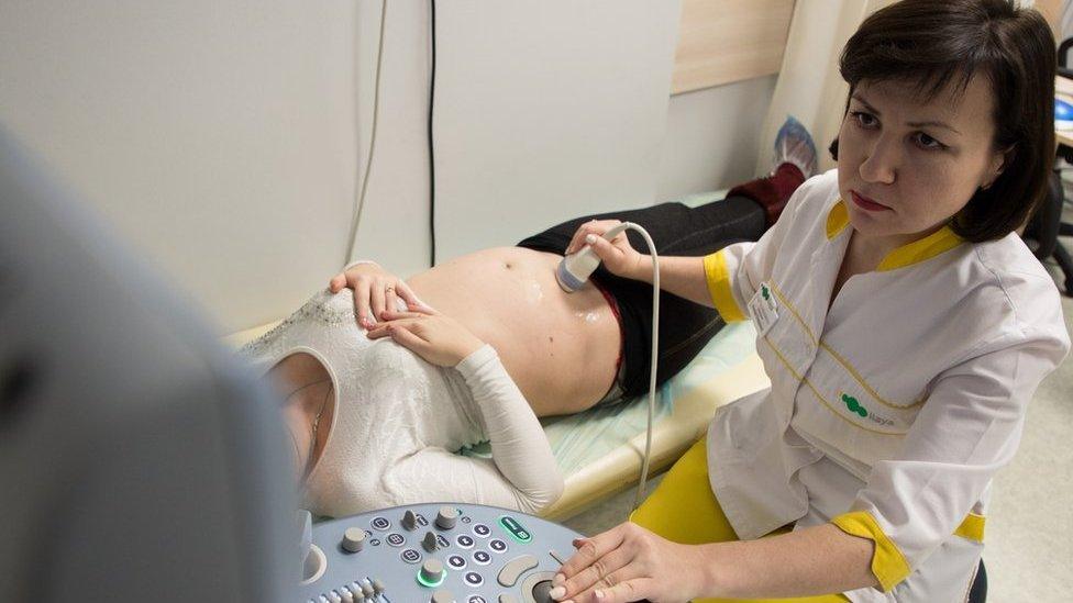 A doctor runs an ultrasound probe over the stomach of a pregnant surrogate at the Ilaya clinic