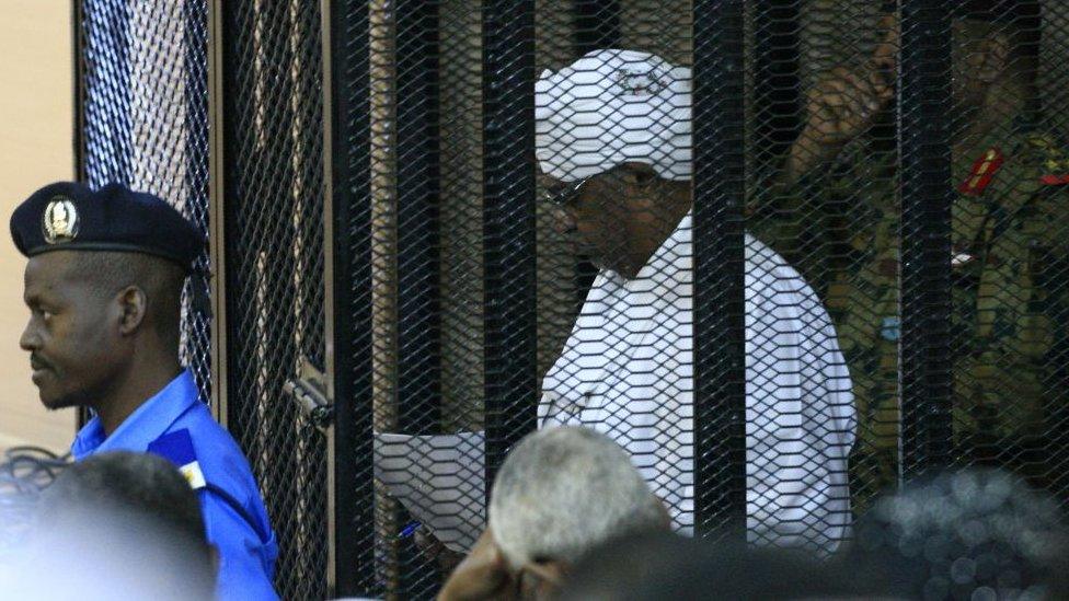 Sudan's deposed military ruler Omar al-Bashir stands in a defendant's cage during the opening of his corruption trial in Khartoum on August 19, 2019