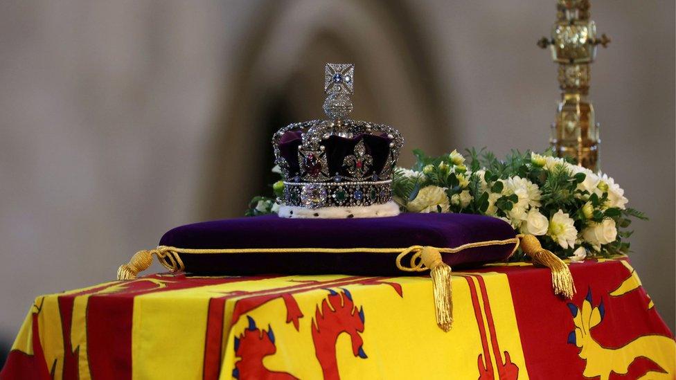 The coffin of Queen Elizabeth II, draped in the Royal Standard with the Imperial State Crown and the Sovereign's orb and sceptre, lying in state on the catafalque in Westminster Hall