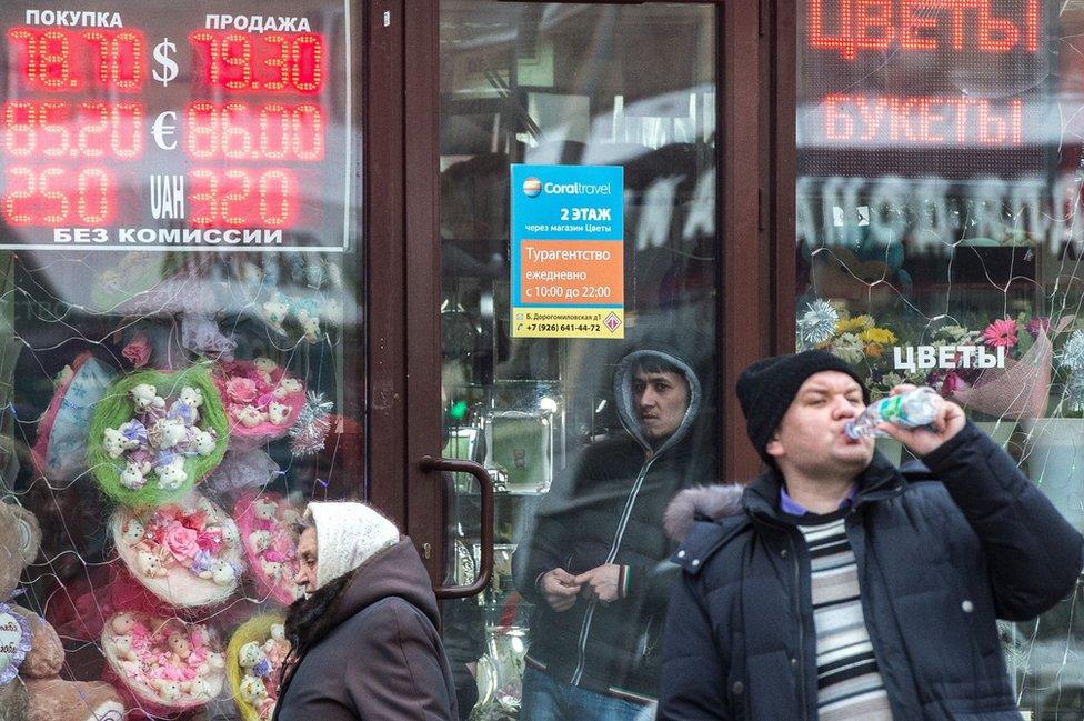 Pedestrians walk past boards listing foreign currency rates against the Russian rouble outside an exchange office in Moscow on 18 January 2016.