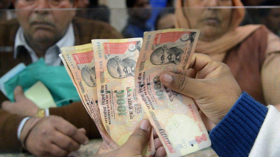 An Indian bank teller counts out notes as senior citizens gather inside a bank as they wait to deposit and exchange 500 and 1000 rupee notes in Amritsar on November 19, 2016.