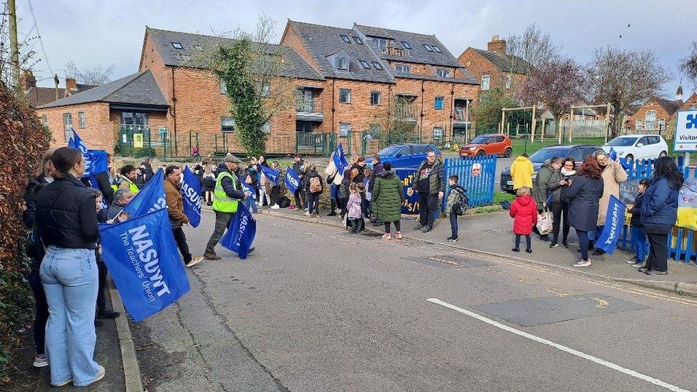 Teachers with blue banners on a road outside a school