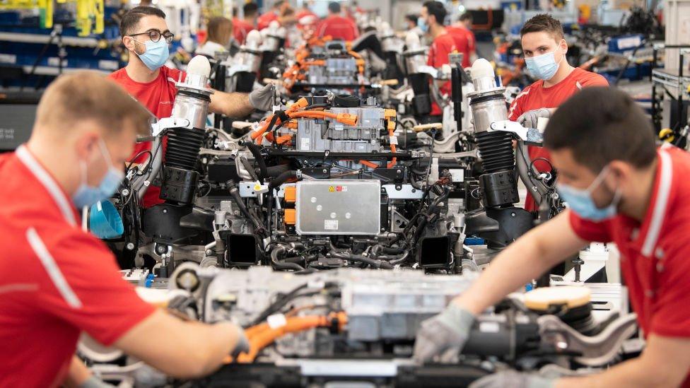 Employees of German car manufacturer Porsche wear face masks as they work on power trains for the Taycan full-electric sportscar at the production site in Stuttgart, southern Germany, on May 12, 2020,