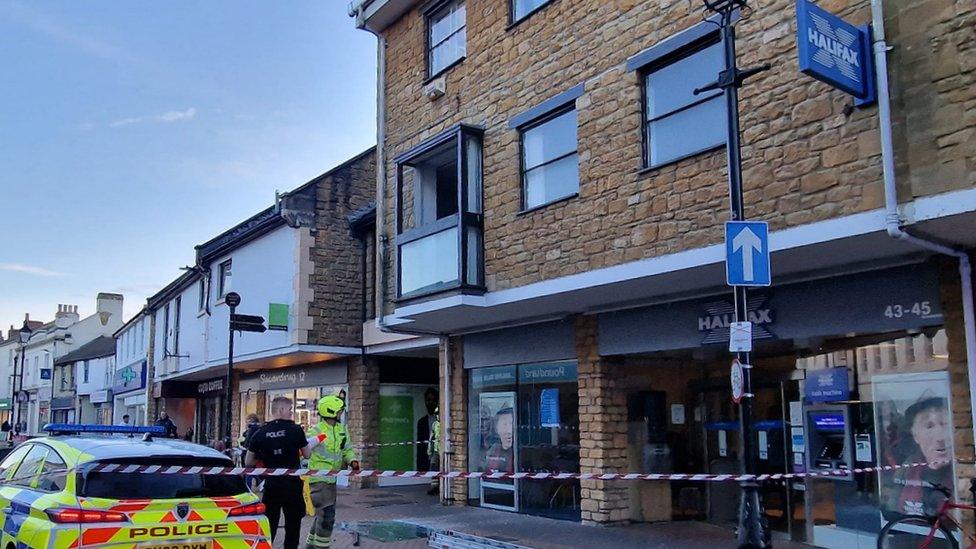 smashed glass on floor outside bank with police around