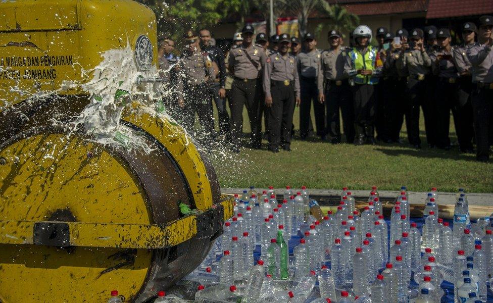 A steamroller crushes bottles of alcohol