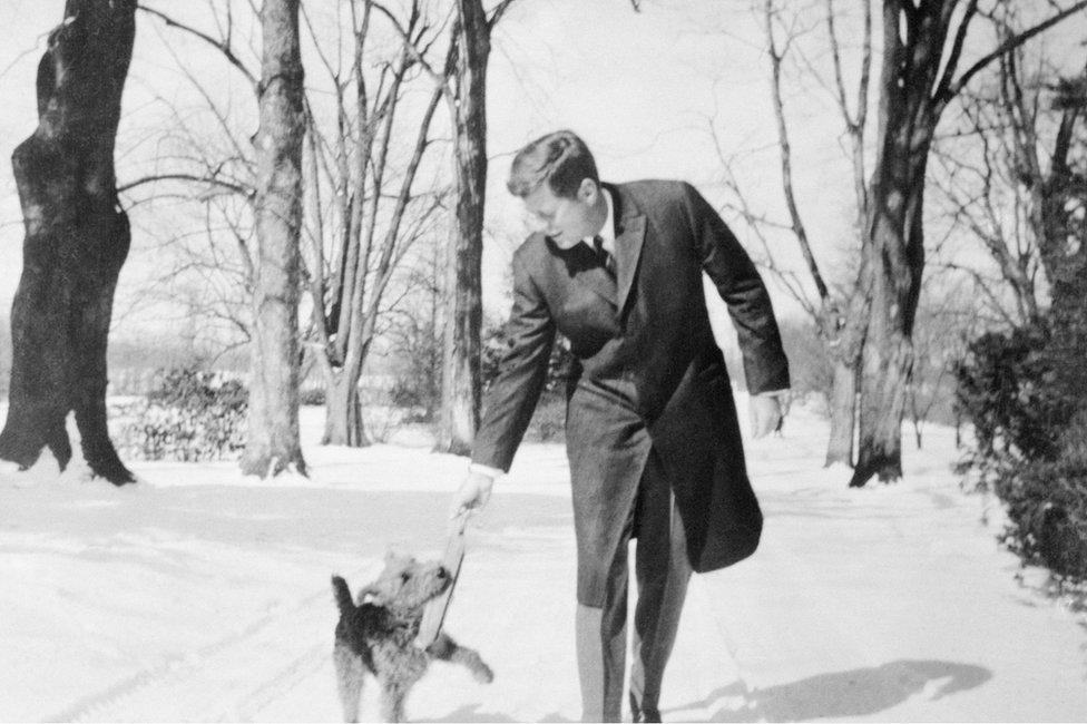 President Kennedy plays with his dog in snowy landscape