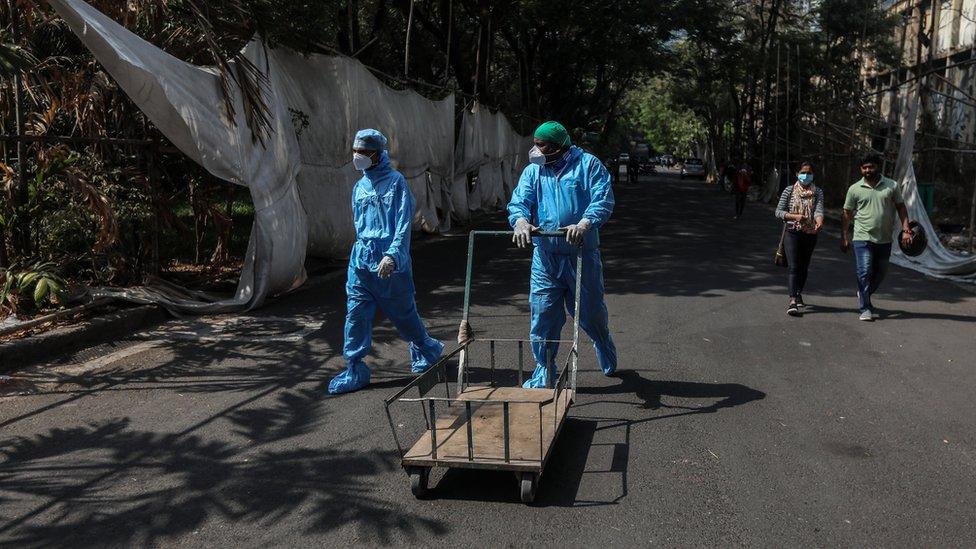 Health workers wearing personal protective equipment walk pass a quarantine centre in Mumbai, India, 12 April 2021.