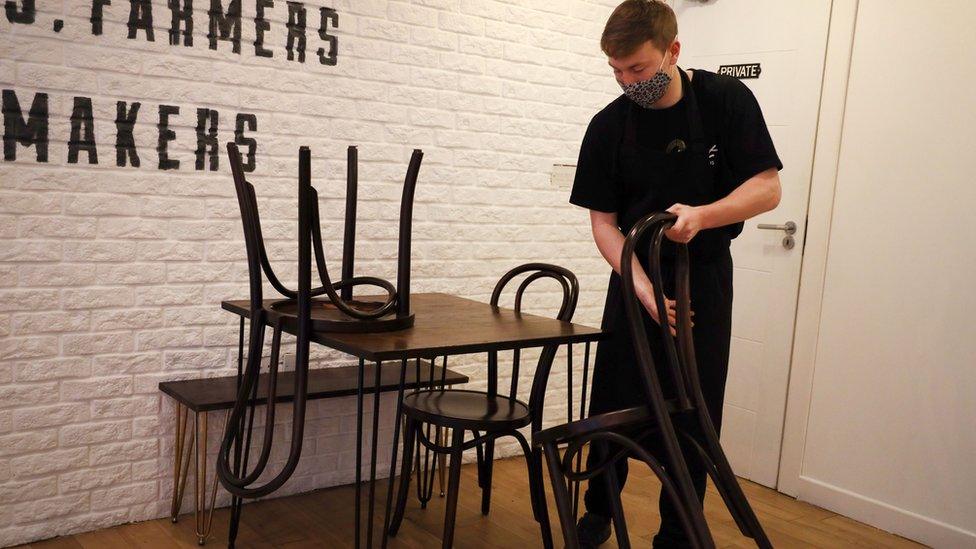 A cafe worker stacks chairs on top of a table