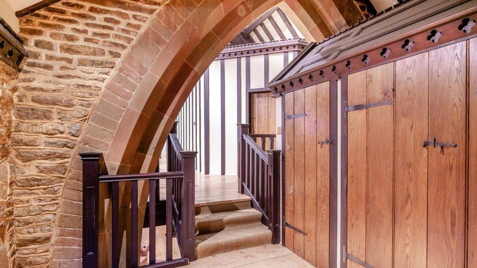 Small staircase between levels in stone and wood house. Part of a stone arch is visible.