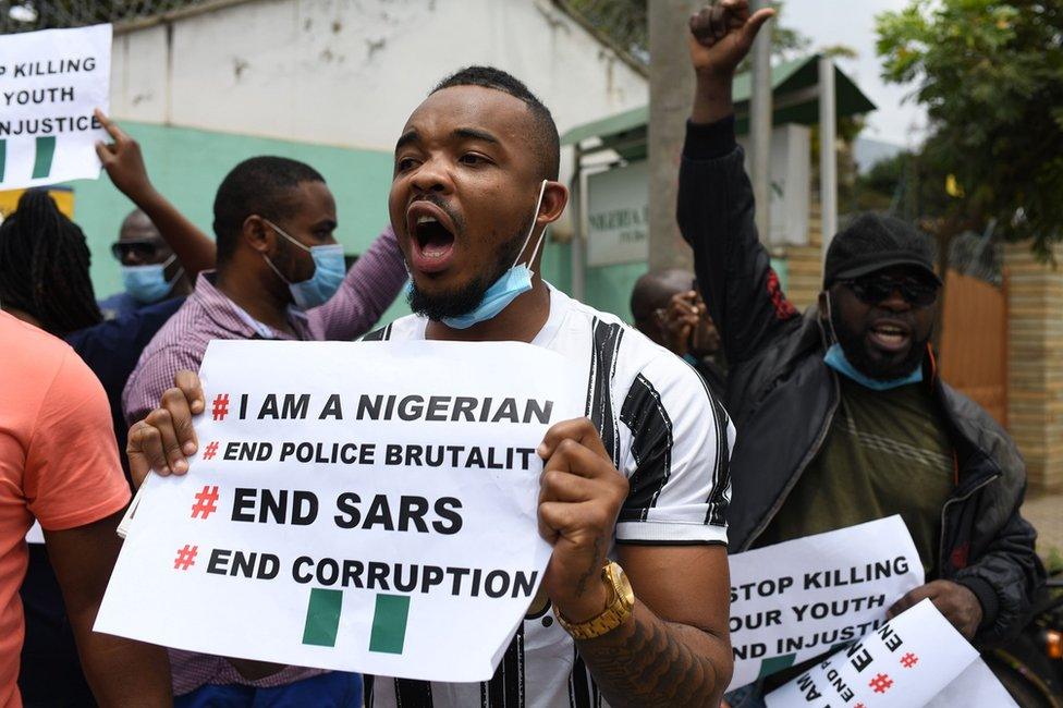 A man holds up a sign as people gather to protest outside the Nigerian embassy in Nairobi