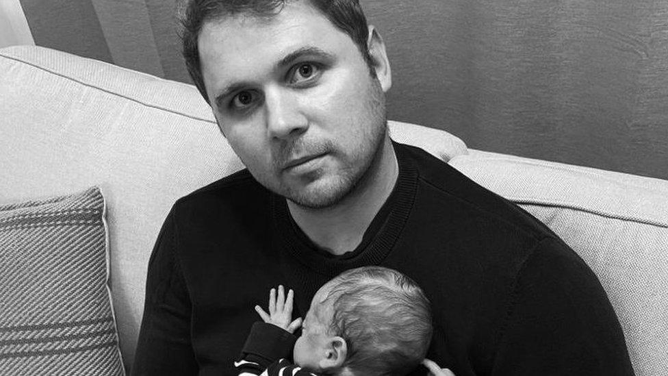 Christopher Jones holding his baby while sitting on a sofa.