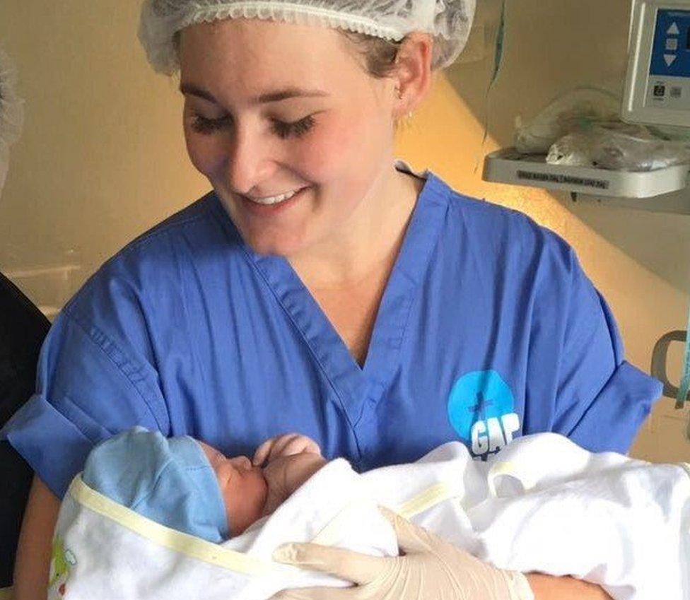 A young woman in nurse scrubs holds a baby