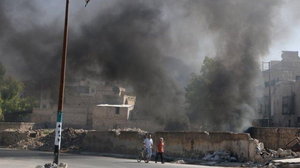 Men walk past burning tyres, which activists said are used to create smoke cover from warplanes, in Aleppo