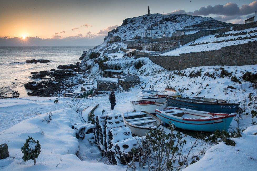 The sun sets as snow covers fishing boats left at Priest's Cove at Cape Cornwall near Penzance on 28 February