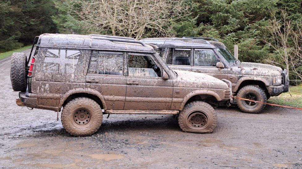 Two mud covered Land Rover-type vehicles