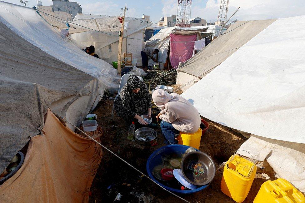 Displaced Palestinians wash utensils at a tented camp in Khan Younis, in the southern Gaza Strip (14 November 2023)