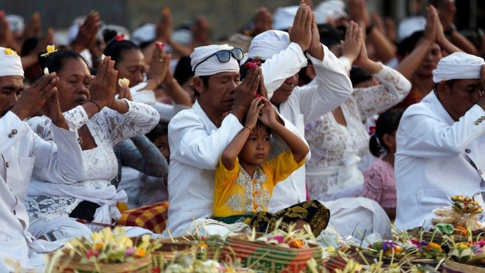 Worshipers are pictured wearing white and praying cross legged.