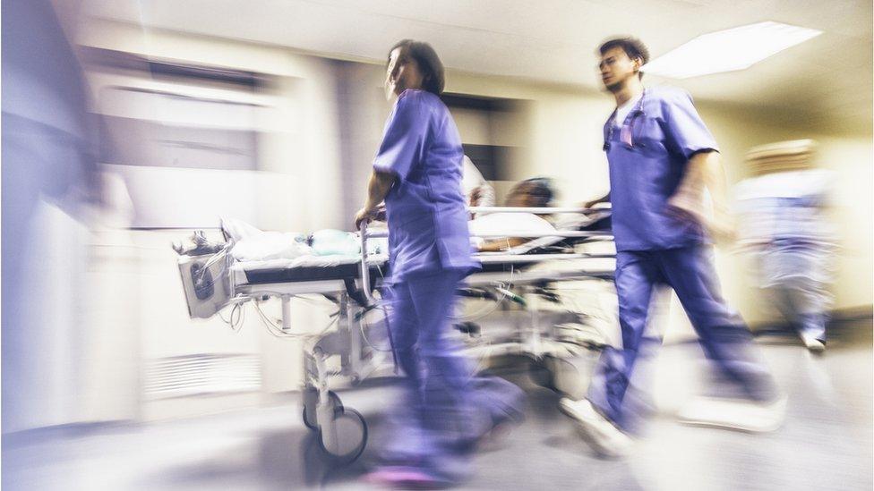 A pair of medical staff rush a patient on a trolley through hospital