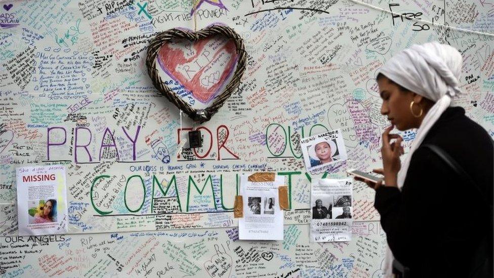 A woman looks at her smartphone in front of a message board near the scene of the fire that destroyed the Grenfell Tower block