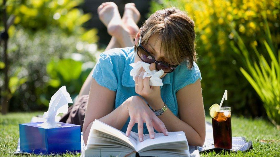 A woman blowing her nose while laying down in her garden