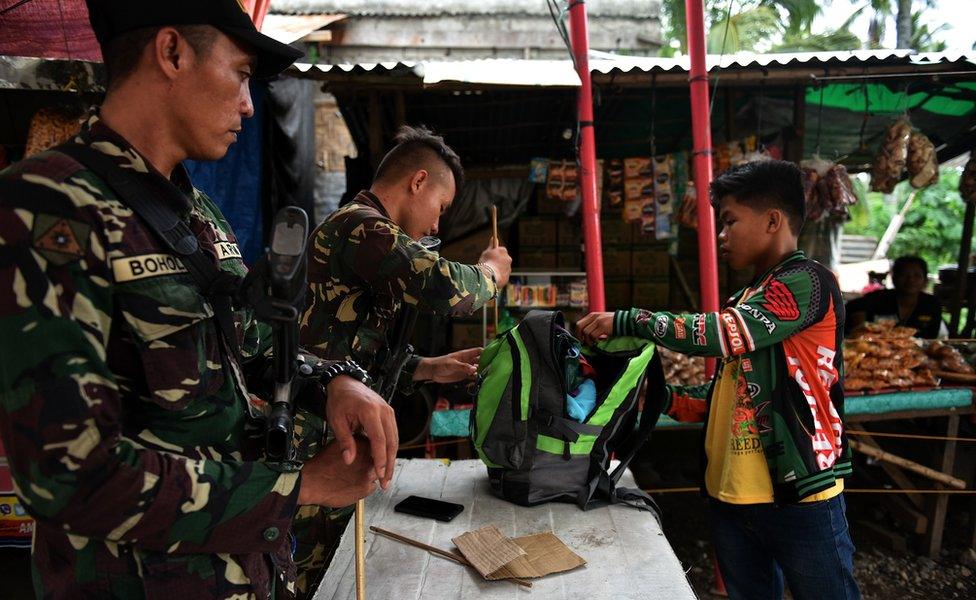 Two members of the security forces in Davao city examine a man's bag at a checkpoint on a road into the city