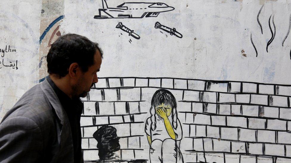 A man walks past a wall covered in graffiti depicting a warplane dropping bombs on child, in Sanaa, Yemen (10 August 2018)