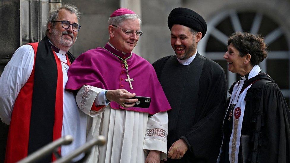 Faith leaders outside the cathedral, one holding a phone as the others smile