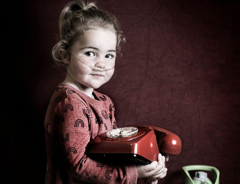 A young girl with a nose tube holds a phone