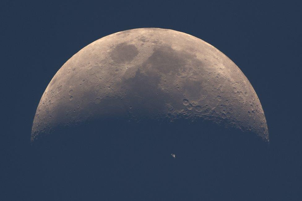 The International Space Station (ISS) whizzes across the dusky face of the moon