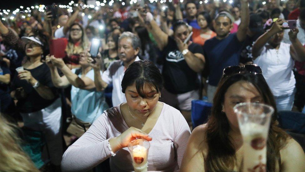 People hold up their phones in lieu of candles at an interfaith vigil for victims of a mass shooting