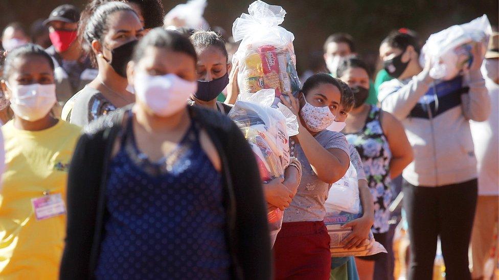 People carry plastic bags with food aid distributed at a favela in Sao Paulo