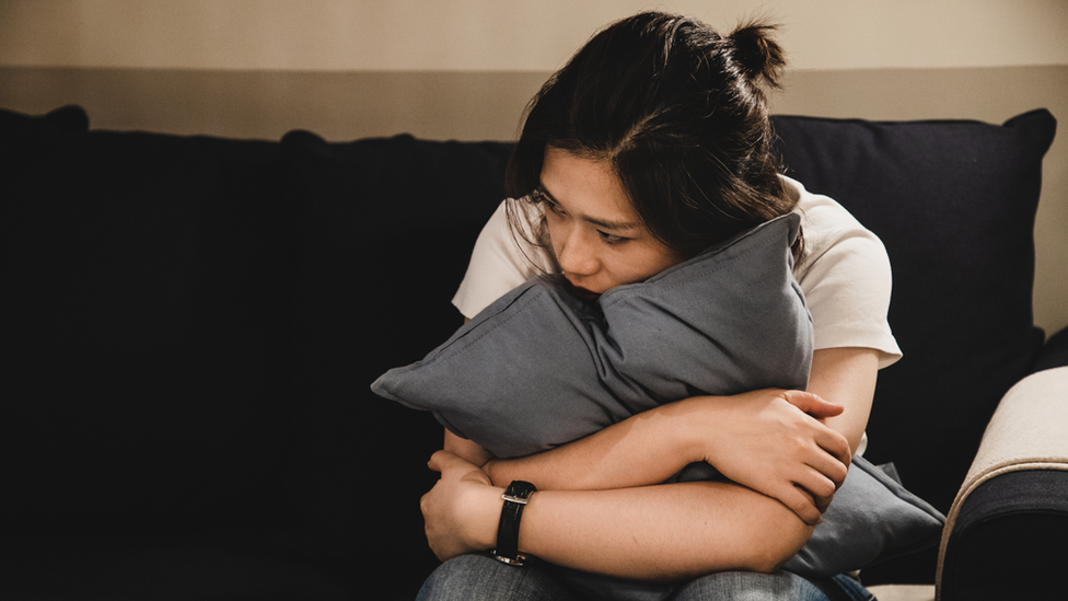 Woman holds pillow looking sad