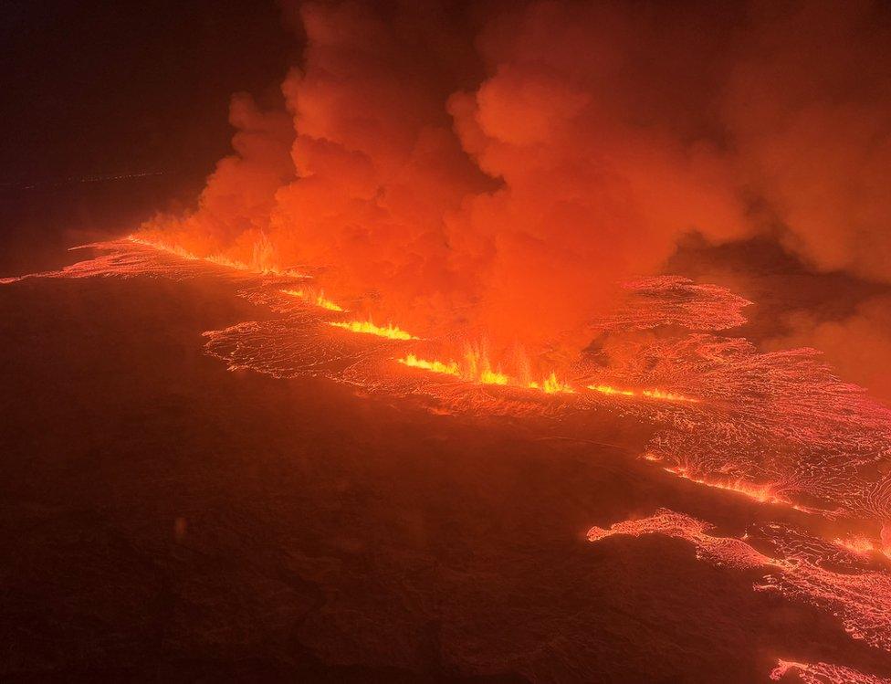 An aerial view of a volcano spewing lava and smoke as it erupts