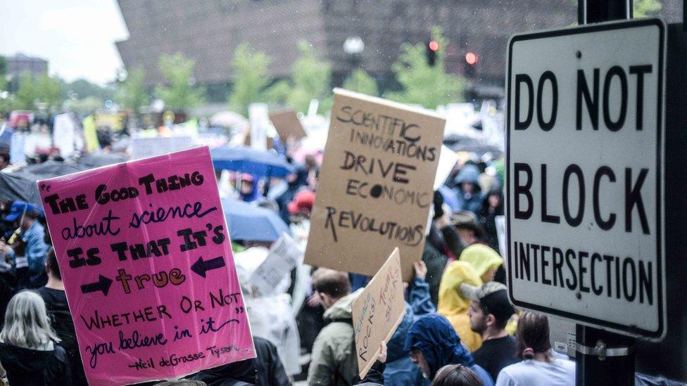 A placard says "The good thing about science is that it's true whether you believe it or not"